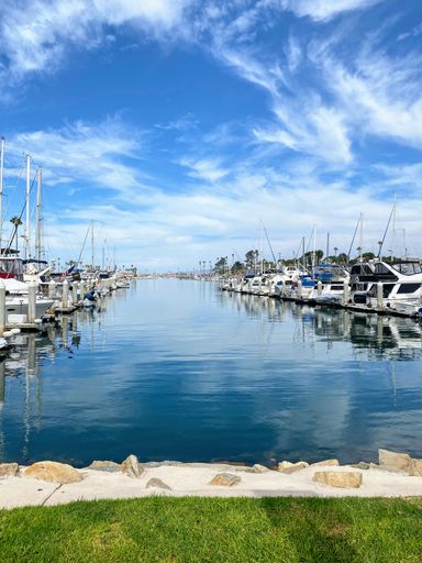 A vertical shot of a harbor with anchored boats in rows under a blue cloudy sky on a sunny day