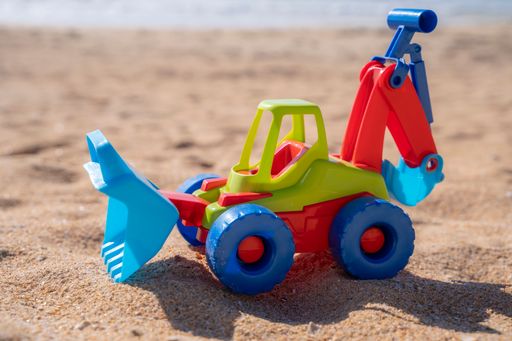 A closeup shot of a toy tractor on the sand at the beach under the sunlight