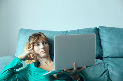 A Caucasian female using a laptop while lying on the sofa at home
