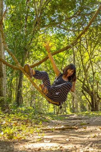 A vertical shot of a woman on the branch of a tree