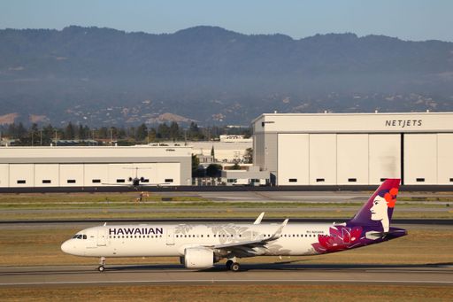 Hawaiian Airlines Airbus A321 neo on runway with NetJets hangar and Santa Cruz mountains in background at San Jose airport.