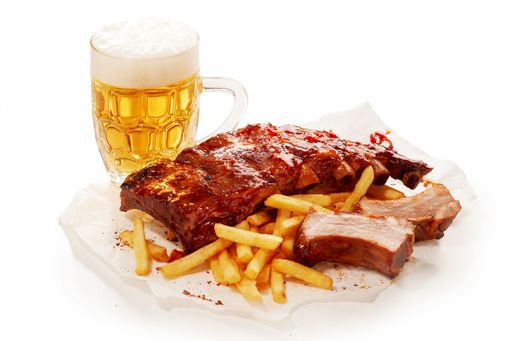 A closeup shot of barbeque pork spareribs and French fries served with a glass of lager beer
