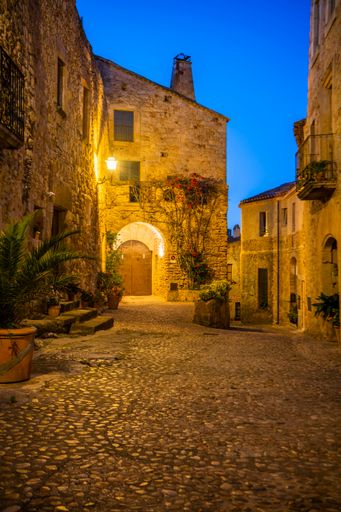 A vertical shot of a medieval town with old rough weathered stone buildings illuminated at night