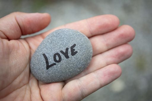 A closeup shot of a man's hand holding a stone with love written on it