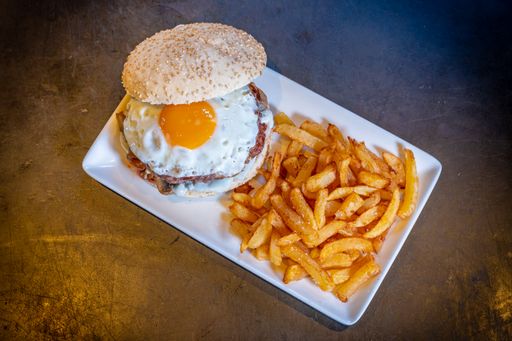 A closeup of a hamburger with a fried egg and french fries on a black background, on a white plate