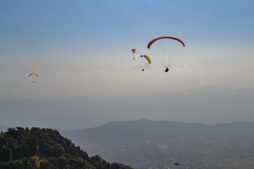 A landscape of hills covered in greenery and fog with people paragliding above at daytime