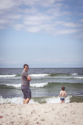 A vertical shot of a male standing on the beach near the sea in Sarbinowo, Poland