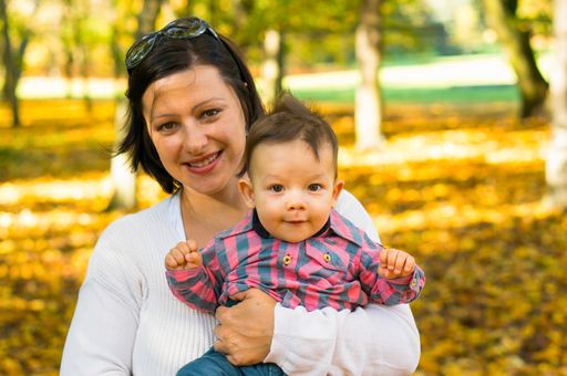 A view of a mother hugging his son on the background of a park on an autumn day