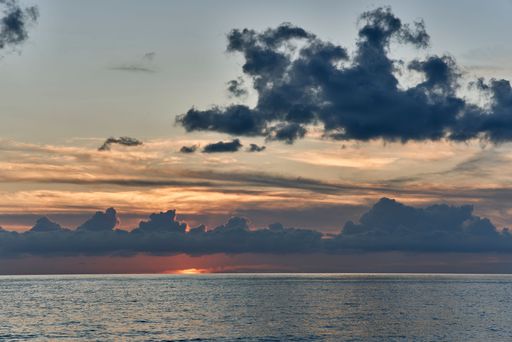 A serene ocean sunset with dramatic clouds and a gradient sky over calm waters.