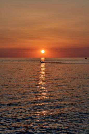 A mesmerizing sunset over the ocean with a small boat silhouetted against the vibrant sky.