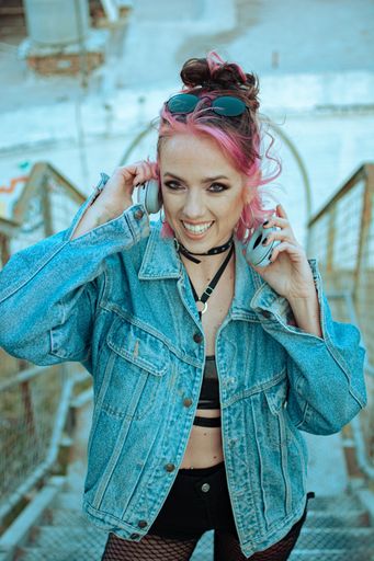 A vertical shot of a cheerful Caucasian lady with pink hair, gothic style clothing and accessories