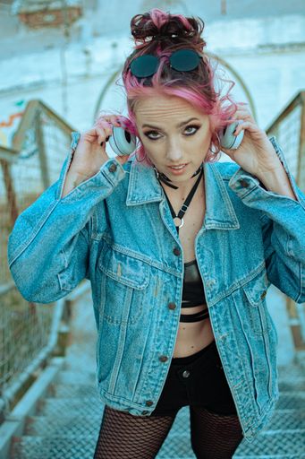 A vertical shot of a cool young Caucasian lady with pink hair, gothic style clothing and accessories