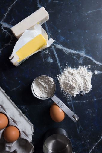 Baking ingredients including butter, flour, and eggs on a dark marble countertop, ideal for culinary and recipe concepts.