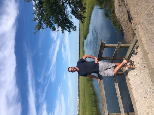 A vertical shot of a male in shorts, sandals, and sunglasses leaning on a wooden rail next to a creek in Mount Pleasant, South Carolina