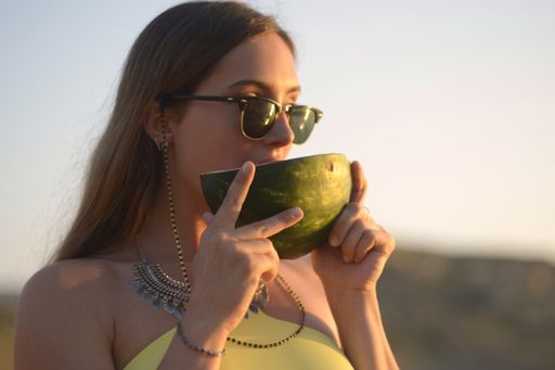A shallow focus shot of a female eating a watermelon slice while wearing sunglasses