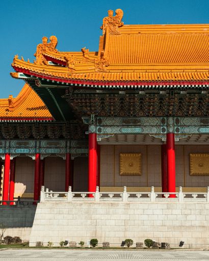 Traditional Chinese architecture with vibrant red columns and ornate roof against a clear blue sky in Taipei.