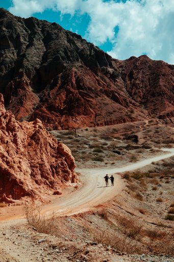 A scenic shot of two people walking on a deserted road surrounded by mountains under the cloudy sky