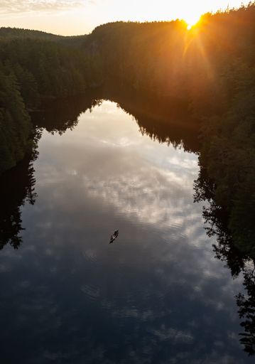 A canoe floats on a peaceful lake at sunset, with cliffs behind it.