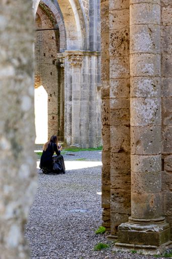 A vertical shot of a female sitting on the ground in Abbey of San Galgano under the sunlight in Italy
