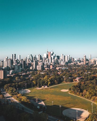Aerial view of Toronto skyline with CN Tower and lush green park in the foreground under a clear blue sky.
