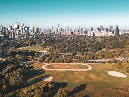 Aerial view of Toronto skyline with lush green park and baseball fields in the foreground under a clear sky.