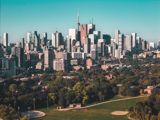 Toronto skyline with CN Tower and urban park in foreground under a clear blue sky.