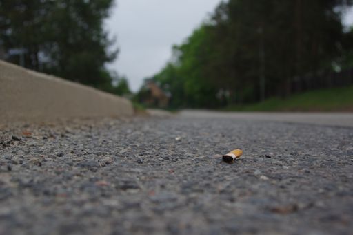 A closeup shot of a used yellow cigarette thrown on the road in the middle of the park