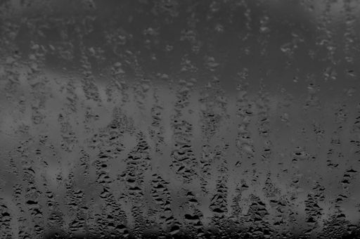 A close-up grayscale shot of a sepia tone window and raindrops falling of it.