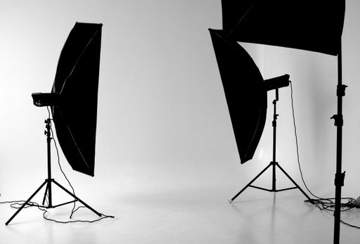 A black and white shot of a photo studio with lighting equipment against a white wall