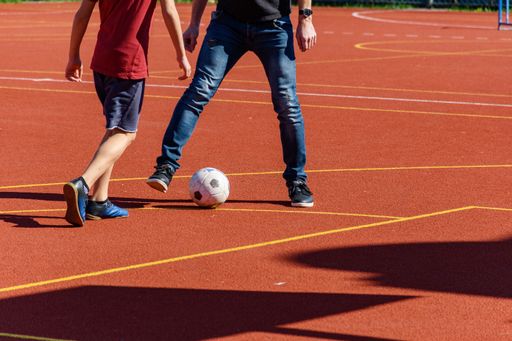 Low section photo of father and son playing soccer or football on orange sports court outdoor