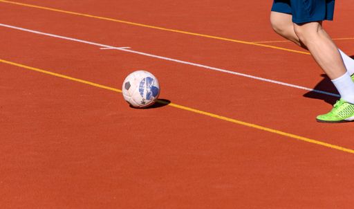 A male athlete playing soccer in a sunny red court