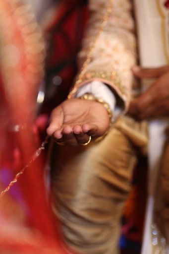 A vertical closeup of a groom in a golden suit holding his hand open during an Indian wedding
