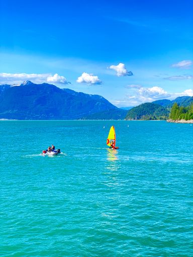 Vibrant scene of windsurfing on a turquoise lake with mountains and clear blue sky in the background, capturing outdoor adventure.