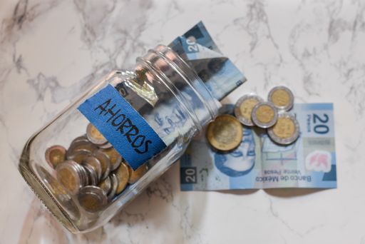 A high angle view of pesos and coins in a jar with a [Ahorros - savings] sticker on it on the table