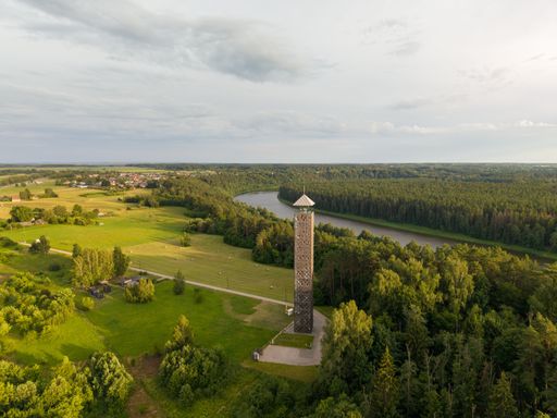 Aerial view of the Birzai observation tower surrounded by lush greenery and a river in Lithuania, showcasing a scenic summer landscape.