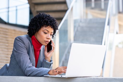 A young African-American businesswoman using her phone and laptop in a business building