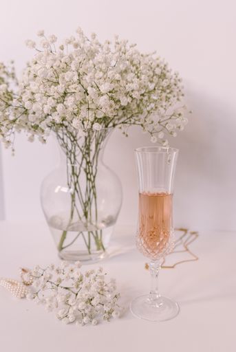 A vertical closeup of a glass of champagne with flowers in a vase on the table on a white background