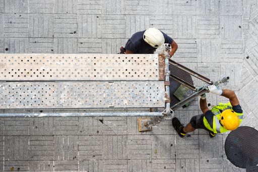 Two construction workers assembling european scaffolding on a city street sidewalk.