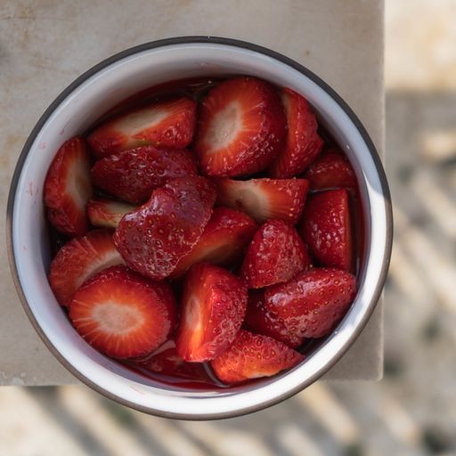 A high angle view of cut strawberries in a metallic bowl on the table with a blurry background