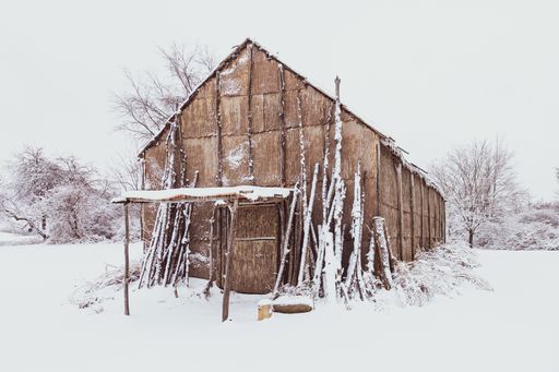 A Native American Longhouse with a ground covered with white snow during winter