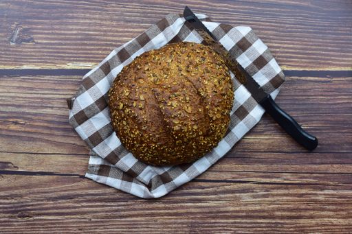 A top view shot of a knife and rye bread on a checkered tower over a rustic wooden background