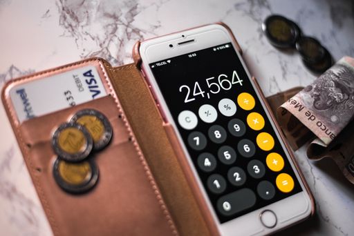 A closeup of a phone with the calculator app on it  with mexican pesos and visa credit card under the lights.