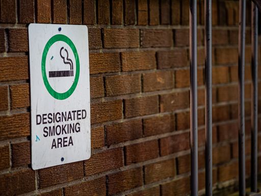 The sign of "Designated Smoking Area" pasted against a brown brick wall