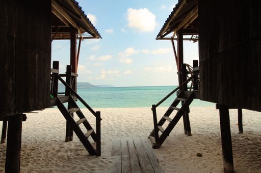 Two stilt bungalow houses framing a breathtaking view of the blue ocean and white sandy beach in Koh Rong Sanloem, Sihanoukville, Cambodia