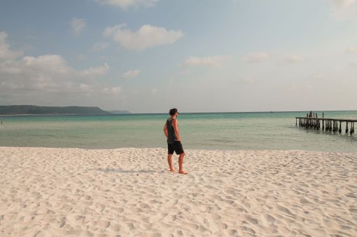 A man stands on a sandy beach looking out at the calm ocean in Koh Rong Sanloem, Sihanoukville, Cambodia