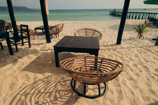Wicker chairs and a table on sandy beach facing the turquoise ocean in Koh Rong Sanloem, Sihanoukville, Cambodia.