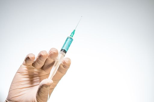 A closeup of a person with a latex glove holding a needle syringe isolated on a white background