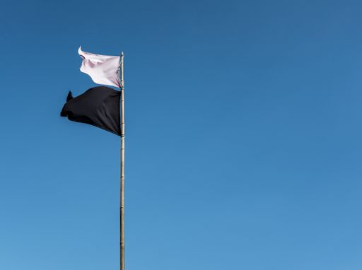 A white flag and a black flag waving on a tall metal pole with a clear blue sky in the background