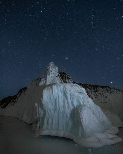A stunning icy landscape at night with a star-filled sky, showcasing a majestic frozen formation in a serene winter setting.