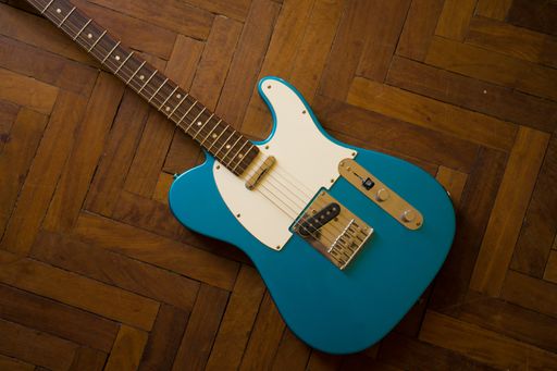 A high angle shot of a blue guitar on a wooden surface